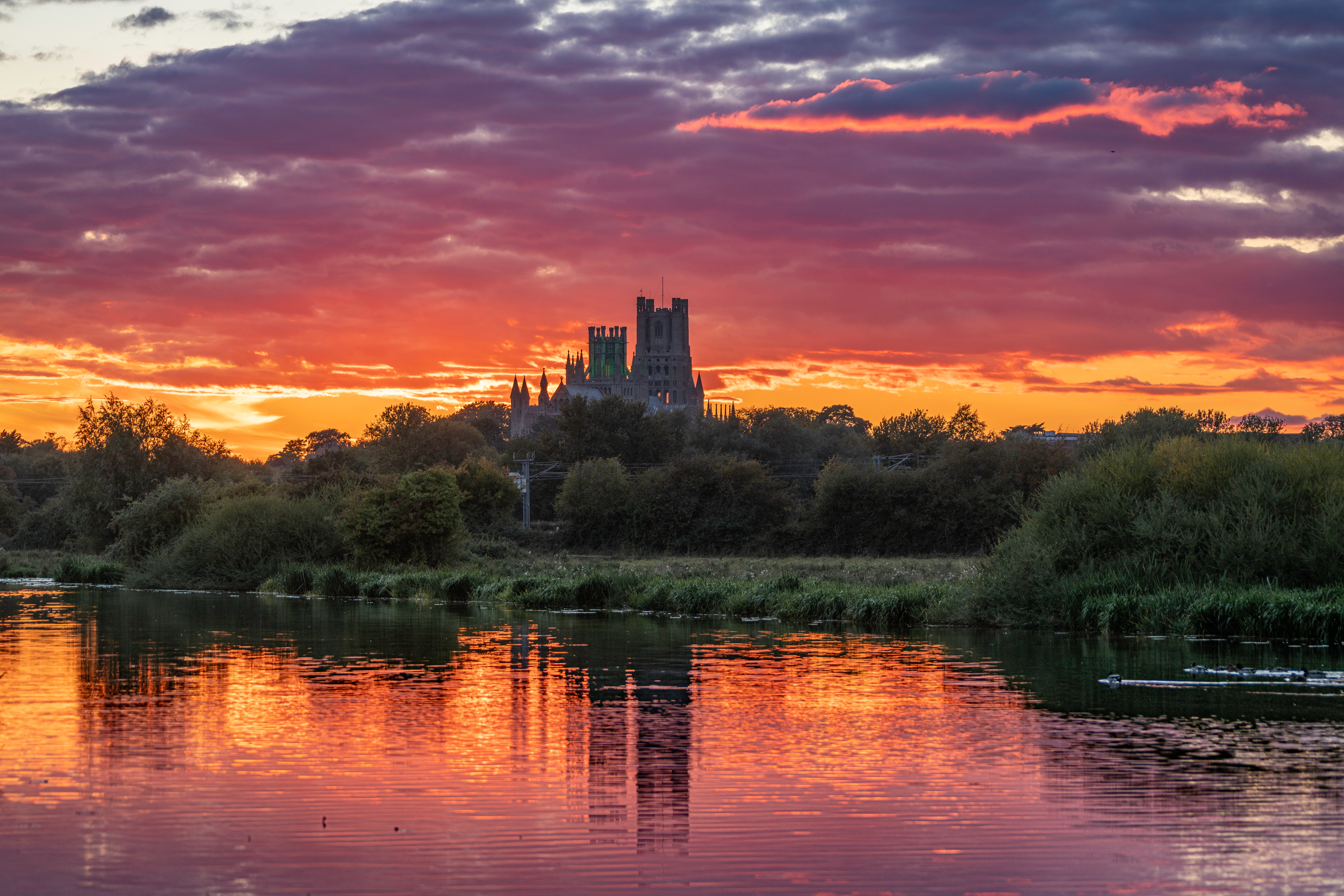 Ely Cathedral beyond the river beneath a dramatic sunset sky