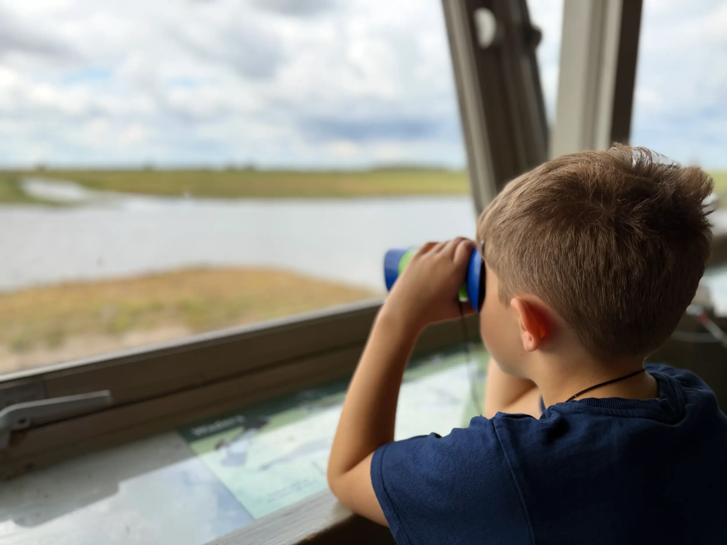A child looking through binoculars from a hide at WWT Welney